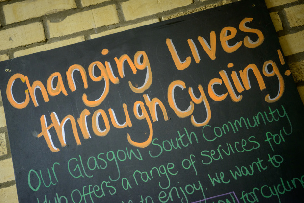 A section of text is written on a blackboard: "Changing lives through cycling! Our Glasgow South Community Hib offers a range of services for..."