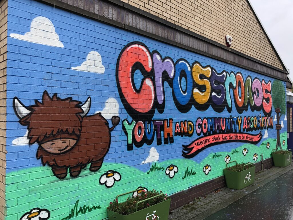 The charity name Crossroads and Youth Community Association is spread across the wall against the backdrop of a pastoral meadow. A quote from the group’s founder, Geoff Shaw, is also included, and reads: “Everyone has the right to live gloriously!”