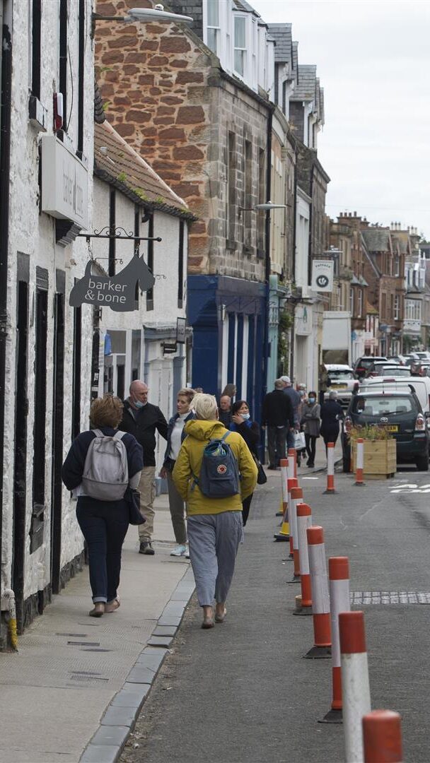 People walk along a street where pavements have been widened using bollards