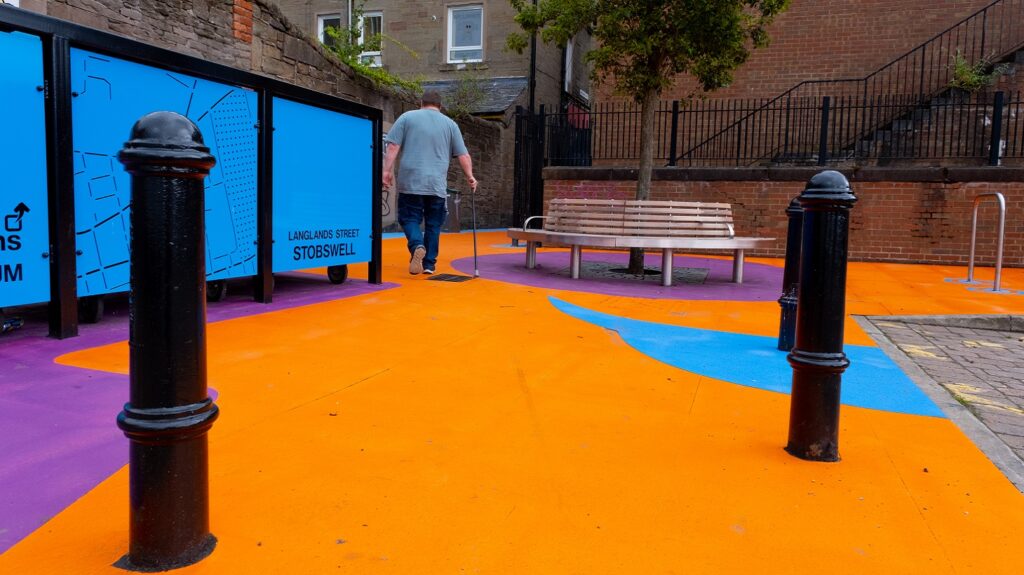 A person is shown walking past a newly installed bench at the opposite end of Langlands Street, walking towards the mural.