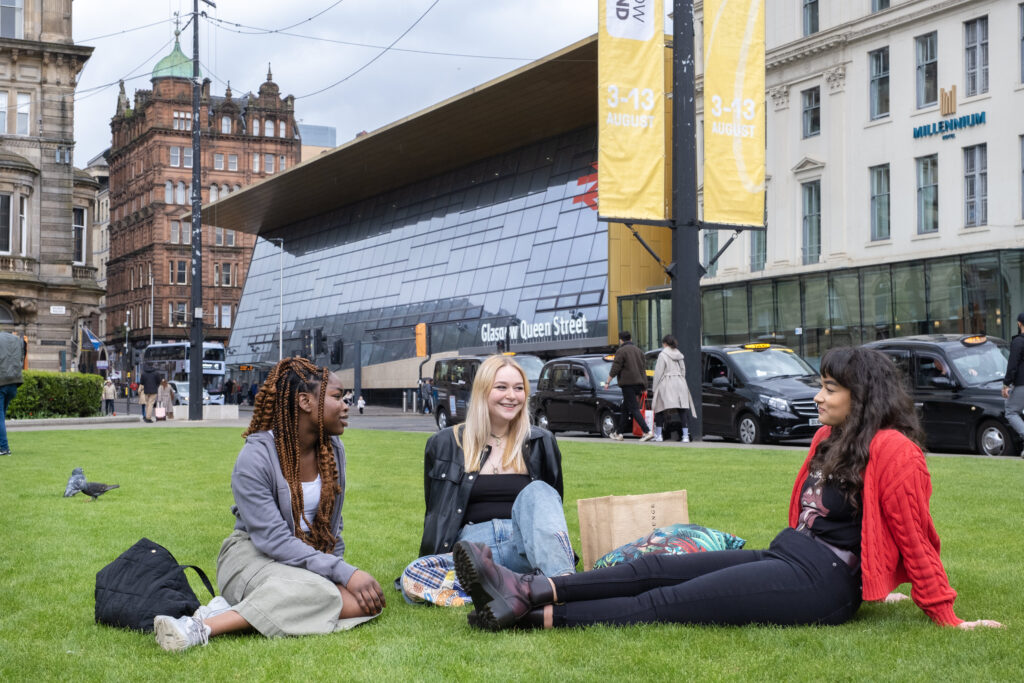 Group of young women sitting in busy public space in Glasgow city centre. 