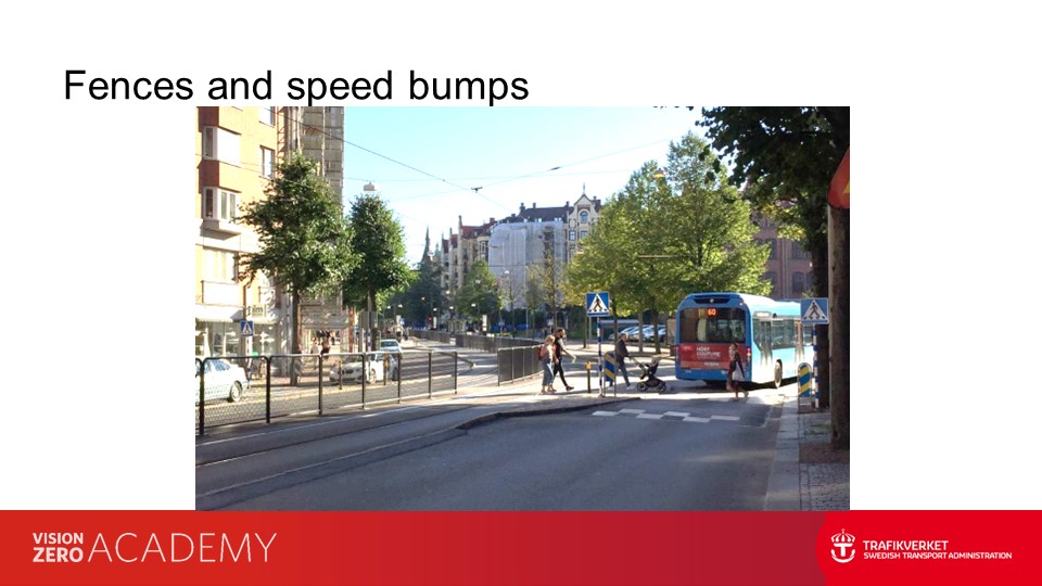 urban area roads separated by fences with frequent gaps for pedestrians, and traffic slowed by speed bumps. 