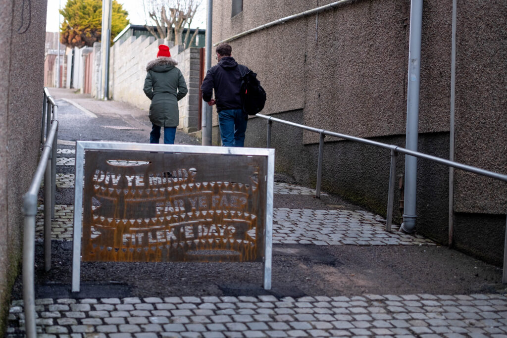 Two people walk by the decorative metal barrier featuring phrases in the Caithness dialect, which has been installed on John Street. Credit: Sustrans