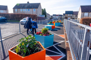 A parent/carer and school pupil walk past planters in the grounds of their primary school.