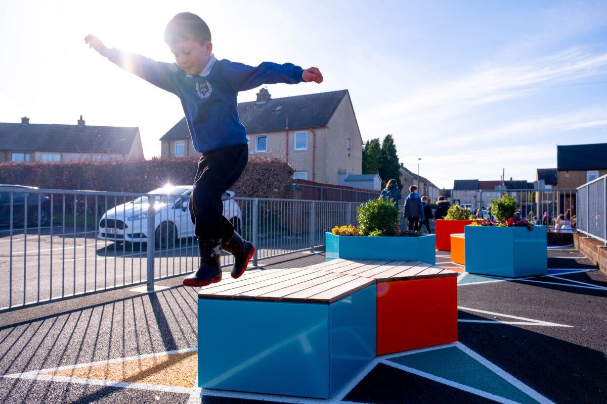 Young boy with brown hair, in school uniform, jumps off of a new playground bench