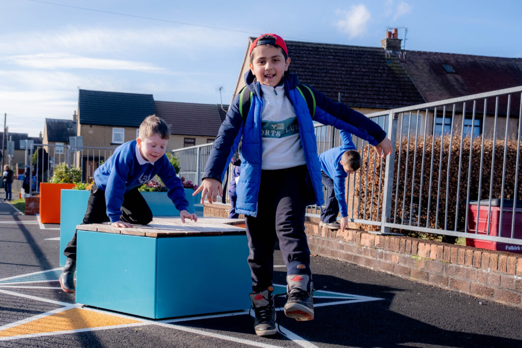 A group of pupils are shown playing on outdoor equipment in the grounds of their primary school.