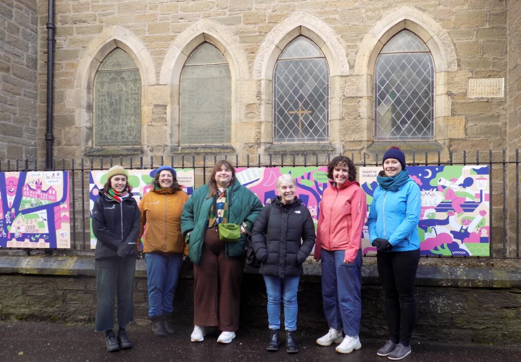 Six people are shown in front of art panels on display outside Stobswell Parish Church.