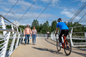 Man on bike cycling across Stockingfield Bridge away from camera. Two pedestrians walk towards the camera in the foreground and a person runs towards the camera in the background